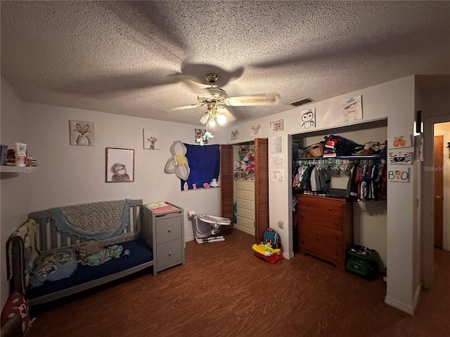 bedroom with dark wood-style floors, a textured ceiling, visible vents, and a ceiling fan