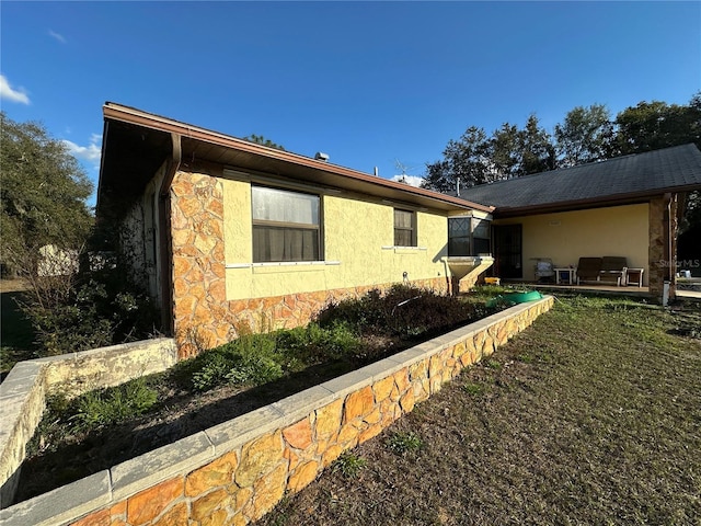 view of side of property featuring stone siding, a yard, and stucco siding