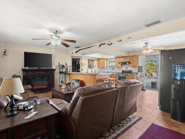 living room with a glass covered fireplace, light tile patterned flooring, visible vents, and ceiling fan