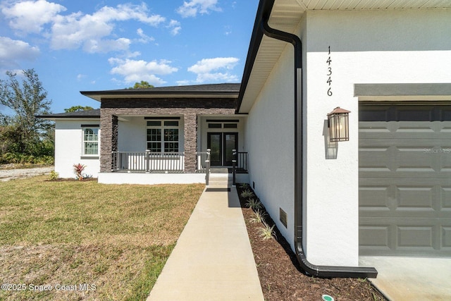 view of exterior entry with an attached garage, covered porch, a lawn, and stucco siding