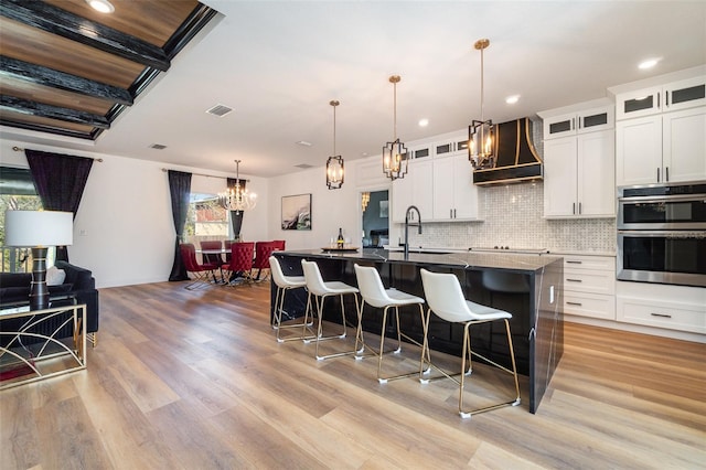 kitchen with premium range hood, a center island with sink, glass insert cabinets, and a sink