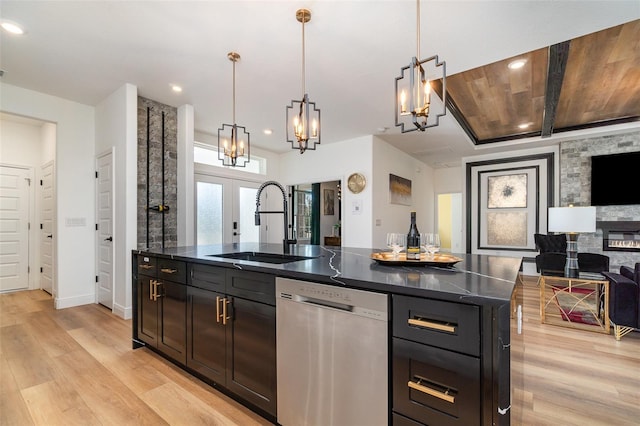 kitchen with dishwasher, dark countertops, hanging light fixtures, a kitchen island with sink, and a sink