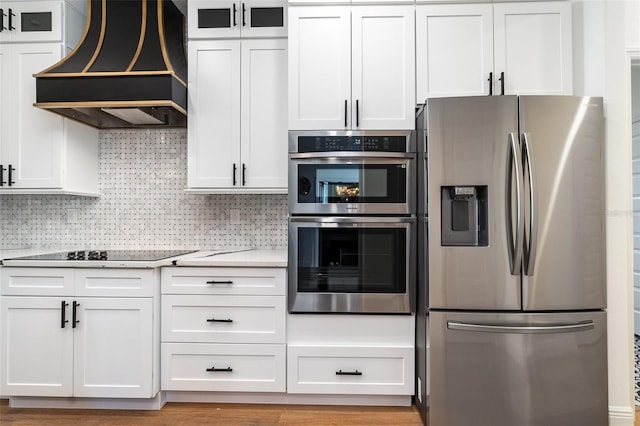 kitchen featuring light stone counters, stainless steel appliances, decorative backsplash, white cabinetry, and premium range hood