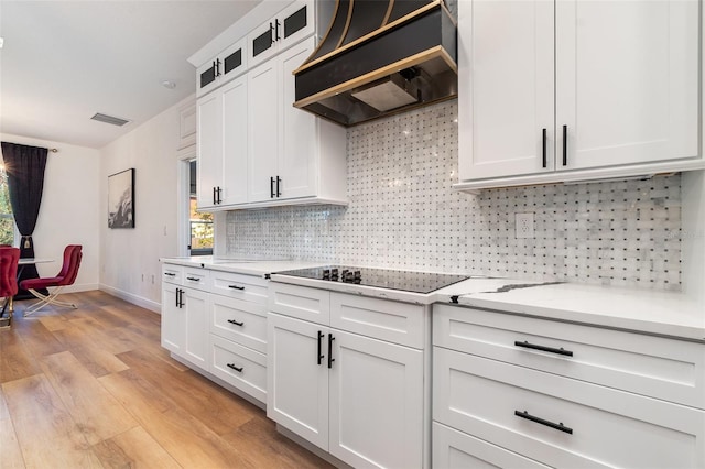 kitchen featuring tasteful backsplash, glass insert cabinets, black electric stovetop, premium range hood, and white cabinetry