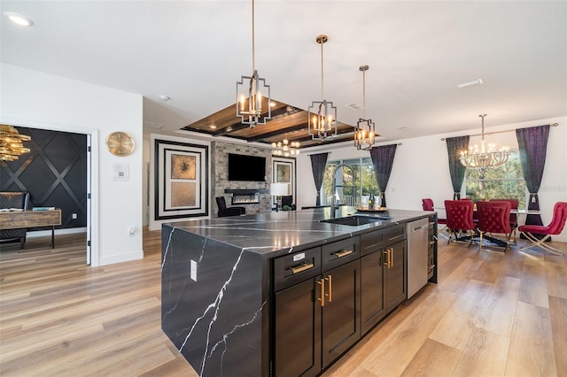 kitchen featuring a kitchen island with sink, a fireplace, a sink, hanging light fixtures, and light wood finished floors