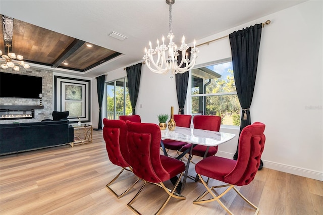 dining space with a chandelier, a large fireplace, baseboards, and light wood-style floors