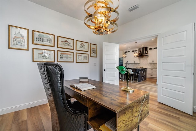 office featuring baseboards, light wood-style flooring, visible vents, and a sink