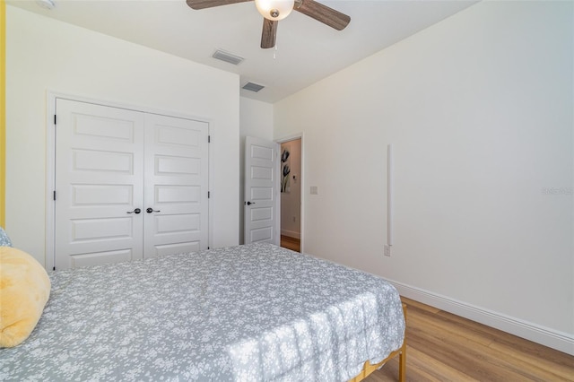 bedroom with baseboards, visible vents, a closet, and wood finished floors