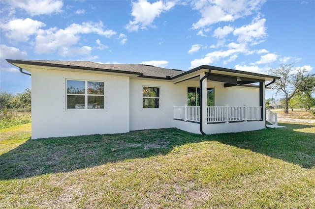 rear view of house with stucco siding, covered porch, and a yard