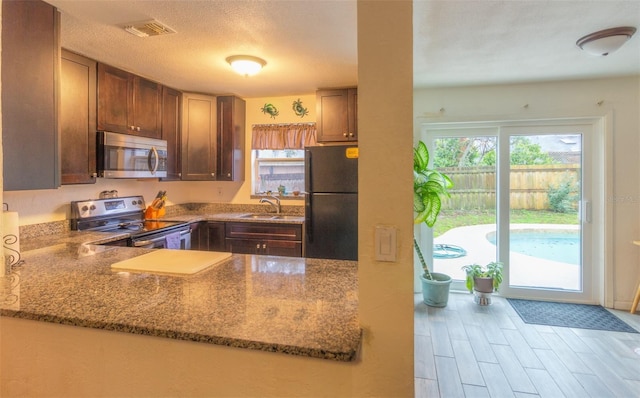 kitchen with stone countertops, a peninsula, a sink, visible vents, and appliances with stainless steel finishes