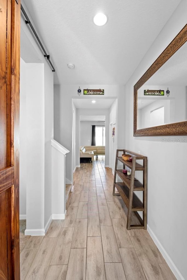 corridor featuring a barn door, baseboards, and wood finish floors