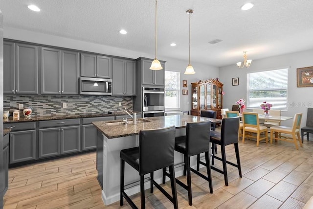 kitchen with appliances with stainless steel finishes, wood finish floors, gray cabinets, and a sink