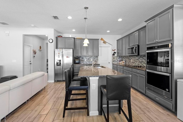 kitchen with stone counters, stainless steel appliances, visible vents, gray cabinetry, and a sink