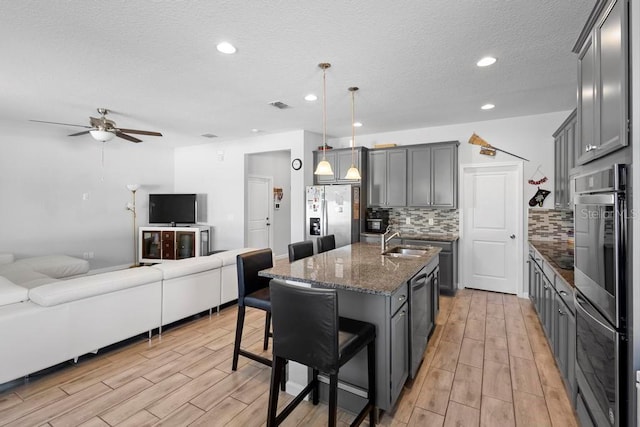 kitchen featuring stainless steel appliances, visible vents, gray cabinetry, open floor plan, and dark stone counters