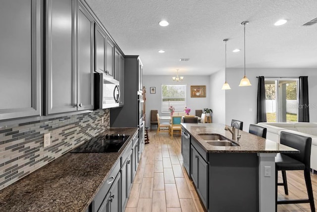 kitchen with decorative backsplash, dark stone counters, appliances with stainless steel finishes, a kitchen breakfast bar, and a sink