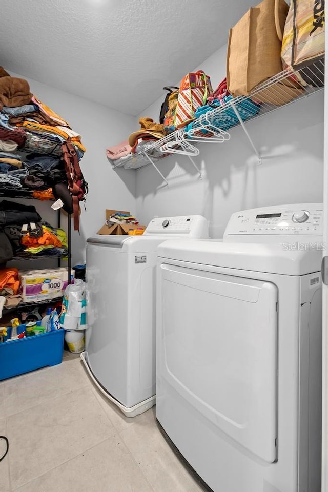 washroom with laundry area, washing machine and dryer, a textured ceiling, and light tile patterned flooring