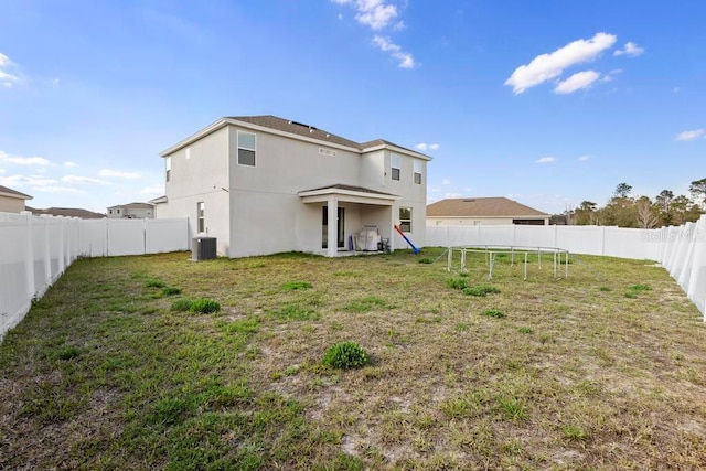 rear view of house with a fenced backyard, central air condition unit, a yard, stucco siding, and a trampoline