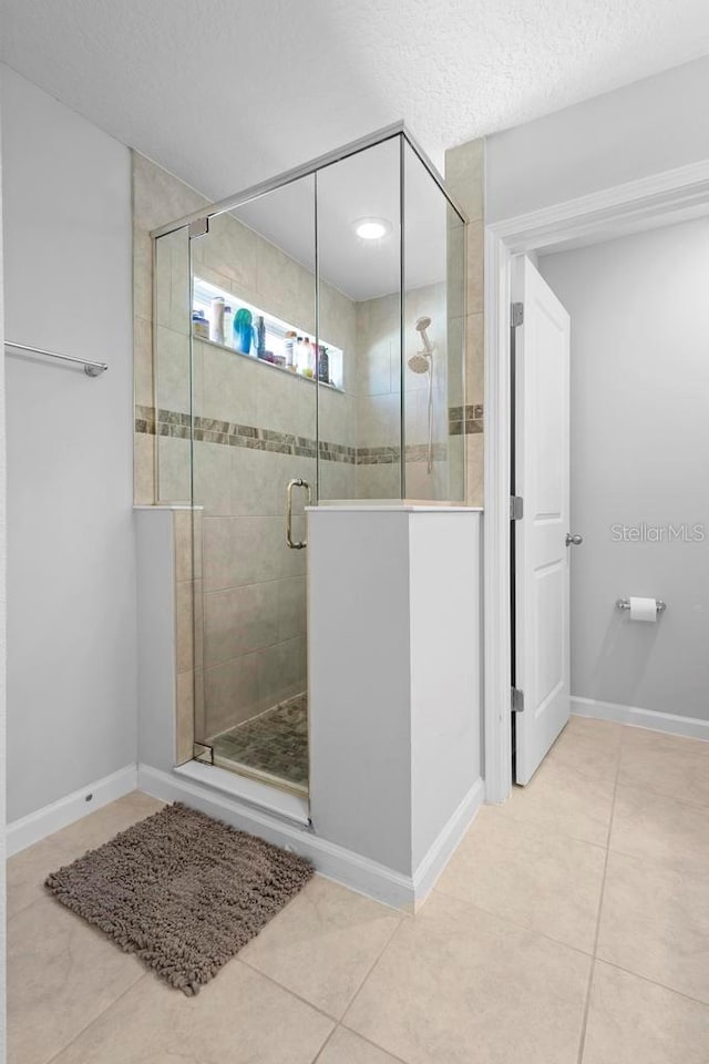 bathroom featuring a shower stall, baseboards, a textured ceiling, and tile patterned floors