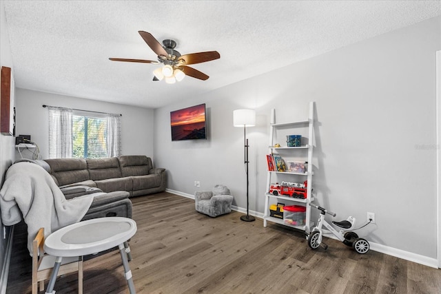 living room with ceiling fan, a textured ceiling, baseboards, and wood finished floors