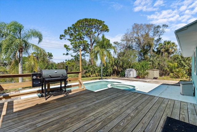 deck featuring a storage shed, a pool with connected hot tub, area for grilling, and an outbuilding