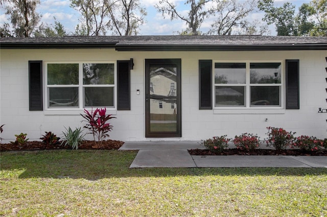 doorway to property featuring concrete block siding, roof with shingles, and a lawn