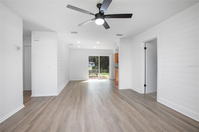 empty room with wooden walls, baseboards, visible vents, a ceiling fan, and wood finished floors