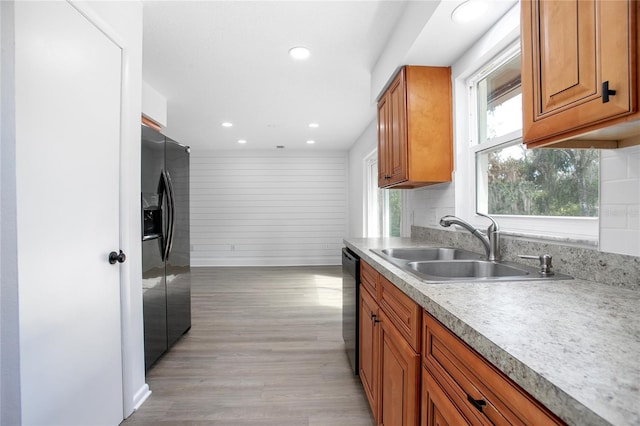 kitchen featuring brown cabinetry, dishwashing machine, light countertops, black fridge, and a sink