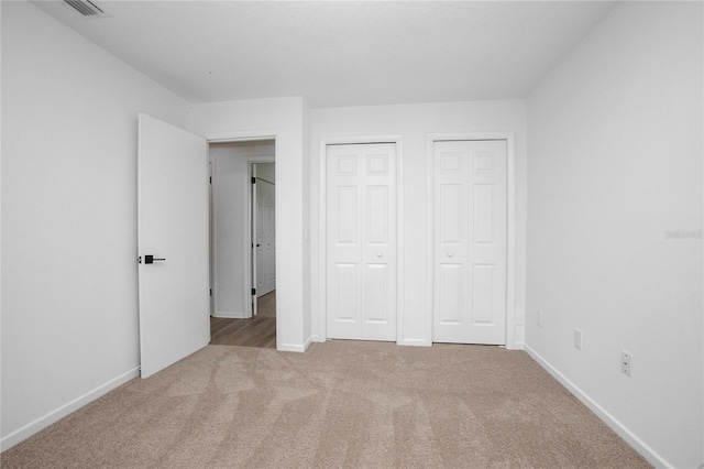 unfurnished bedroom featuring multiple closets, carpet flooring, visible vents, and baseboards