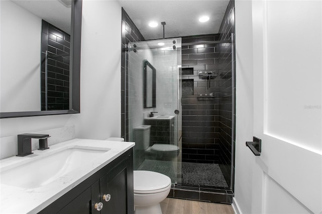 bathroom with toilet, a stall shower, a textured ceiling, vanity, and wood finished floors