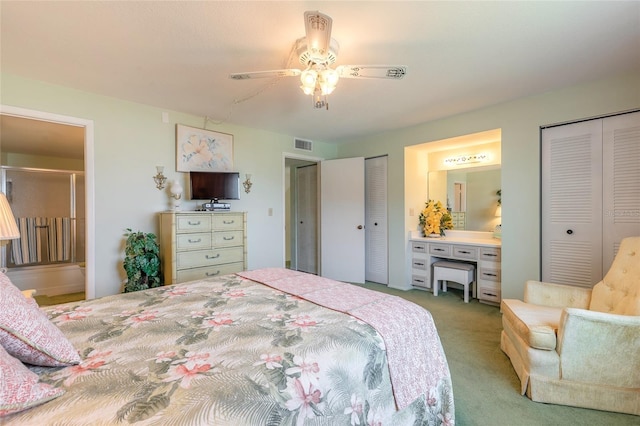 carpeted bedroom featuring connected bathroom, visible vents, ceiling fan, and two closets