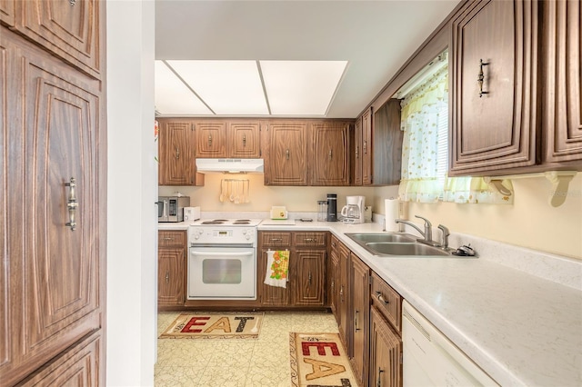 kitchen with light floors, light countertops, a sink, white appliances, and under cabinet range hood