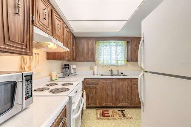 kitchen with white appliances, brown cabinetry, light countertops, under cabinet range hood, and a sink