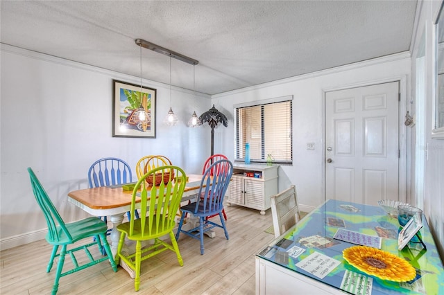 dining space featuring baseboards, light wood-style flooring, ornamental molding, and a textured ceiling