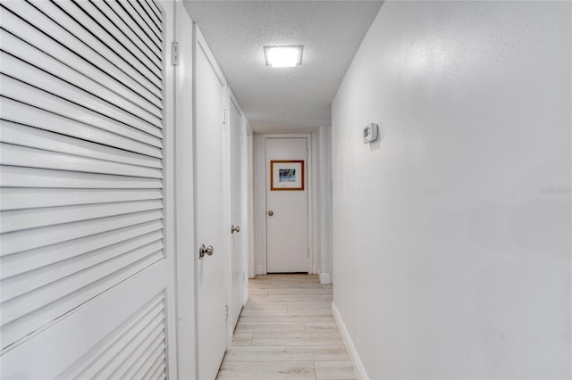 corridor with a textured ceiling, baseboards, and light wood-style floors