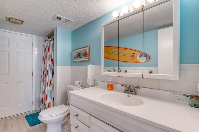 full bath with tile walls, visible vents, toilet, a textured ceiling, and vanity