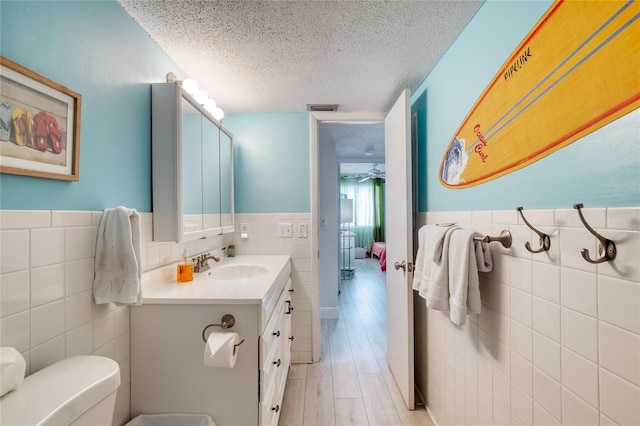 bathroom with tile walls, visible vents, toilet, a textured ceiling, and vanity