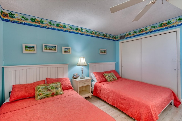 bedroom featuring ceiling fan, a textured ceiling, wood finished floors, visible vents, and a closet