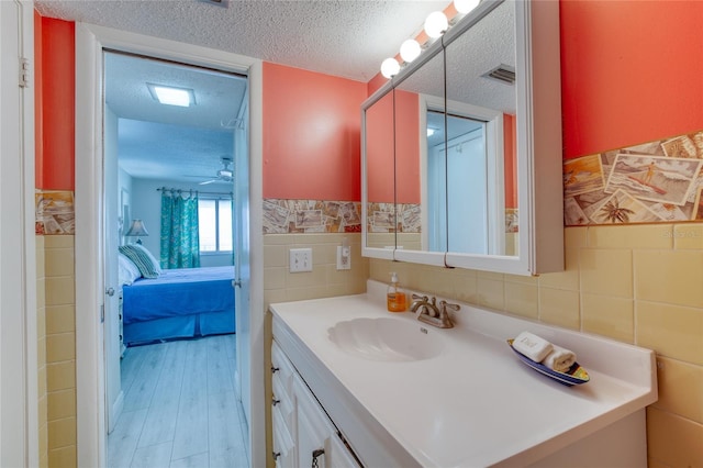 ensuite bathroom featuring tile walls, wainscoting, a textured ceiling, ensuite bath, and vanity