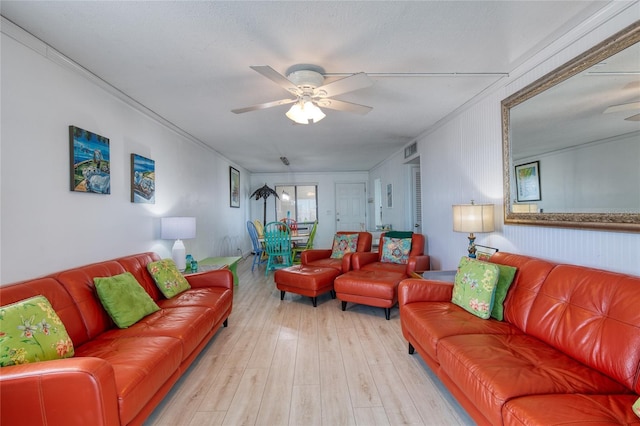 living room with ceiling fan, ornamental molding, visible vents, and light wood-style flooring