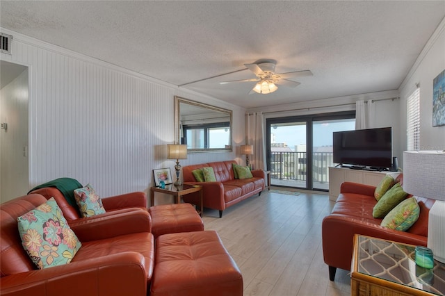 living room with light wood-style floors, a ceiling fan, a textured ceiling, and ornamental molding