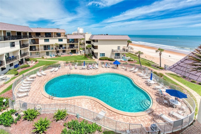 pool with a water view, fence, a beach view, and a patio