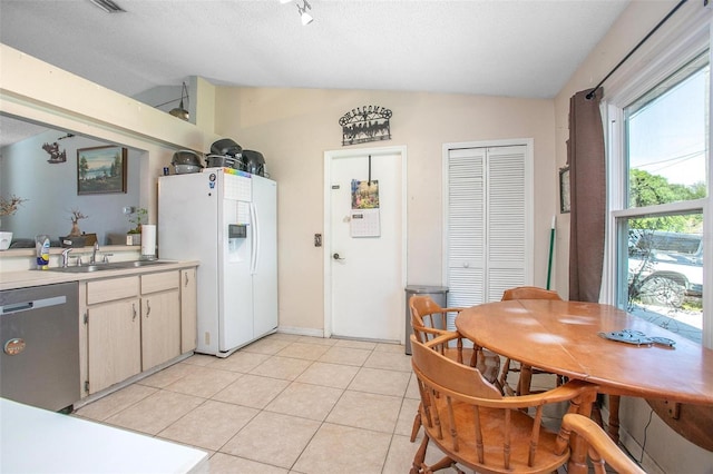 kitchen featuring white refrigerator with ice dispenser, lofted ceiling, stainless steel dishwasher, a sink, and light tile patterned flooring