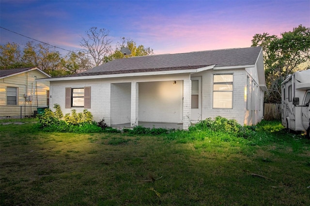 rear view of property featuring a yard, fence, and brick siding