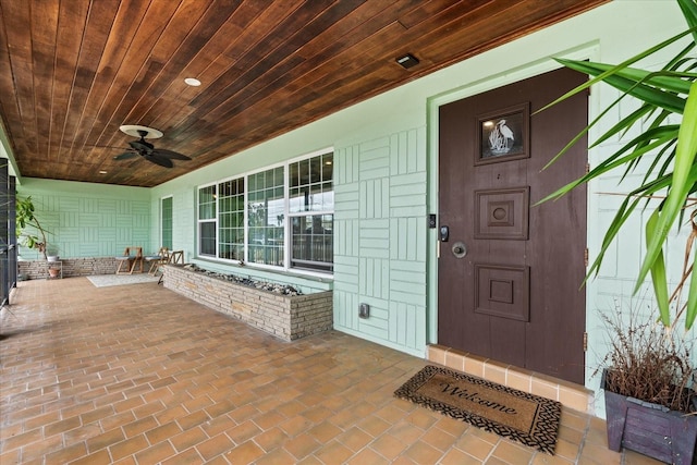 view of exterior entry featuring covered porch, brick siding, and a ceiling fan