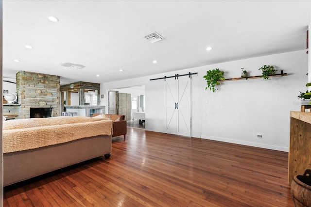 bedroom with a barn door, recessed lighting, a fireplace, visible vents, and wood-type flooring