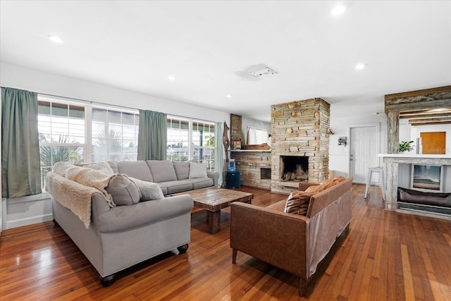 living area featuring recessed lighting, wood-type flooring, and a stone fireplace