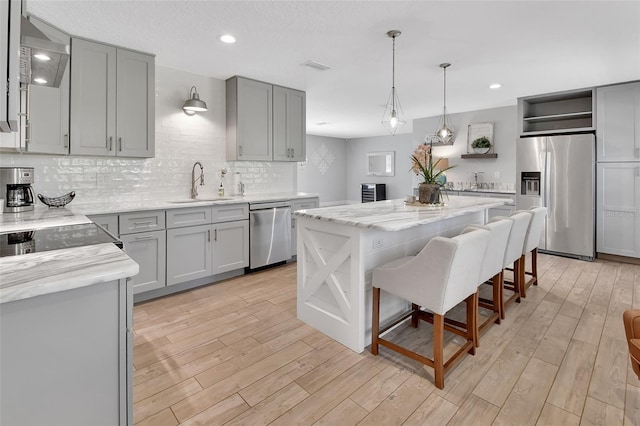 kitchen featuring open shelves, gray cabinetry, appliances with stainless steel finishes, a sink, and light wood-type flooring