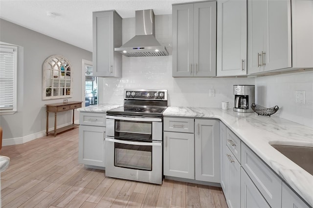 kitchen featuring wall chimney range hood, range with two ovens, light wood-style flooring, and gray cabinetry