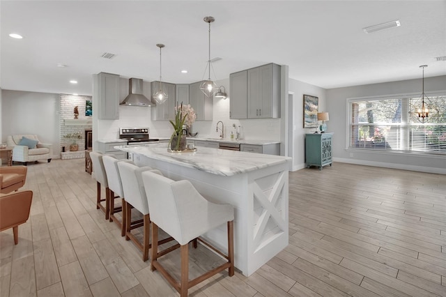 kitchen featuring open floor plan, stainless steel appliances, gray cabinetry, wall chimney range hood, and a sink