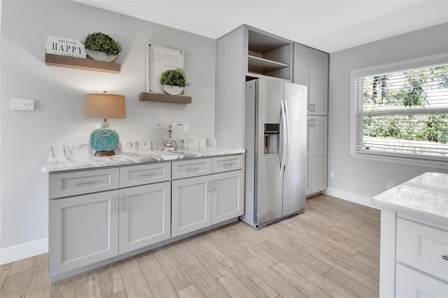 kitchen featuring light wood-style floors, stainless steel refrigerator with ice dispenser, baseboards, and open shelves